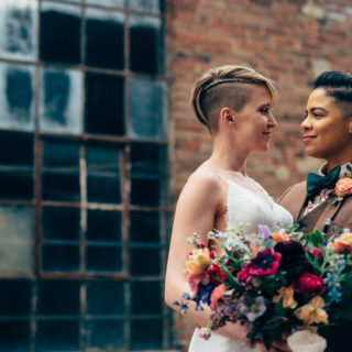 A lesbian couple wearing a dress and a suit smile at each other at Strongwater wedding in Columbus Ohio